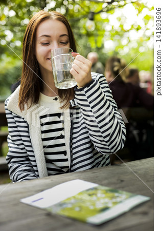 Young woman drinking from a glass mug at an Austrian heuriger, illustrating local winemaker traditions during the growing season. Young woman drinking from a glass mug at an Austrian heuriger, illustrating local winemaker traditions during the growing season. 141893696