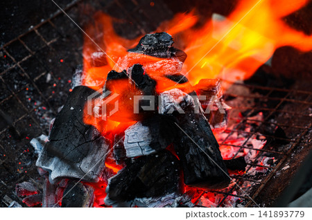 Close-up of burning charcoal with bright orange flames in a barbecue grill. Close-up of burning charcoal with bright orange flames in a barbecue grill. 141893779
