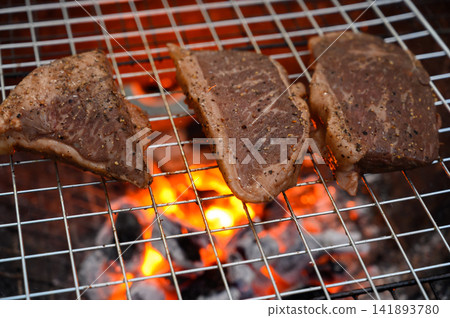 Grilled beef steak cooking on a charcoal fire. BBQ moments that bring people together. Grilled beef steak cooking on a charcoal fire. BBQ moments that bring people together. 141893780