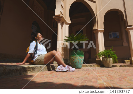 Woman relaxing in sun at historic Tangier courtyard with backpack and potted plants Woman relaxing in sun at historic Tangier courtyard with backpack and potted plants 141893787