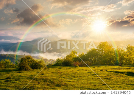 sunset over carpathian mountain landscape with fog. outdoor adventure image for stunning view of meadow. mountain field and rolling countryside valley. cloudy sky with rainbow for background sunset over carpathian mountain landscape with fog. outdoor adventure image for stunning view of meadow. mountain field and rolling countryside valley. cloudy sky with rainbow for background 141894045