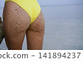 Girl in a yellow swimsuit on a background of the ocean 141894237