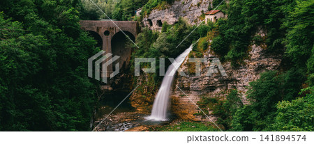 Waterfall in Lush Forest Gorge with Stone Arch Bridge Waterfall in Lush Forest Gorge with Stone Arch Bridge 141894574