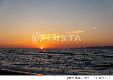 Vibrant orange sunset over ocean waves with distant island silhouette Vibrant orange sunset over ocean waves with distant island silhouette 141894627