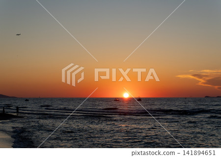 Bright orange sun sets on ocean horizon line with distant boats Bright orange sun sets on ocean horizon line with distant boats 141894651