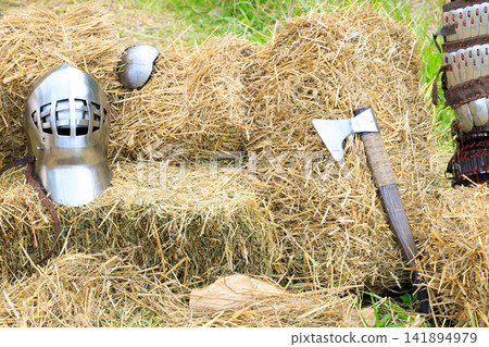 Medieval knight's steel helmet and axe resting on hay bales Medieval knight's steel helmet and axe resting on hay bales 141894979