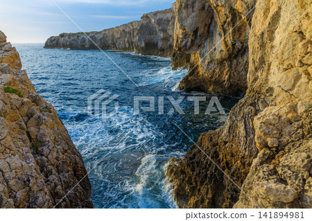 Rugged coastal cliffs meet the deep blue sea with crashing waves Rugged coastal cliffs meet the deep blue sea with crashing waves 141894981