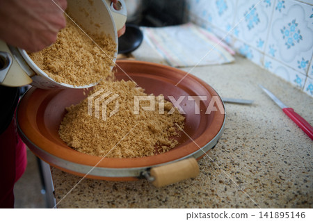 Authentic Moroccan couscous being prepared in a clay tagine by a woman pouring semolina Authentic Moroccan couscous being prepared in a clay tagine by a woman pouring semolina 141895146