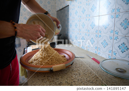 Preparing authentic Moroccan couscous in a home kitchen with hands pouring semolina into a plate Preparing authentic Moroccan couscous in a home kitchen with hands pouring semolina into a plate 141895147