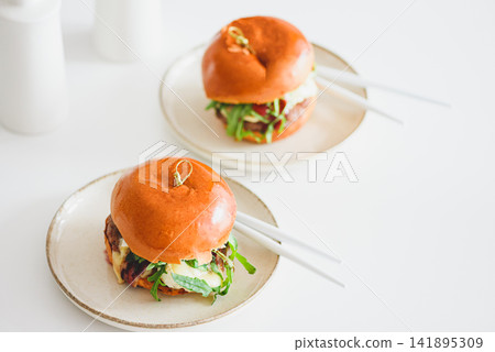 Two gourmet burgers with fresh ingredients served on minimalist plates with chopsticks ready for meal Two gourmet burgers with fresh ingredients served on minimalist plates with chopsticks ready for meal 141895309