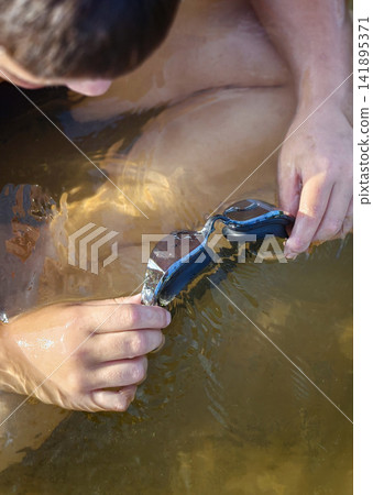 Boy holds swimming goggles in shallow water during summer Boy holds swimming goggles in shallow water during summer 141895371