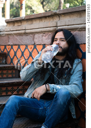 Man drinking water bottle sitting on stairs Man drinking water bottle sitting on stairs 141895563
