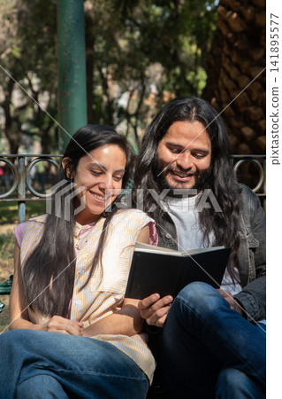 Happy couple reading book together in park Happy couple reading book together in park 141895577
