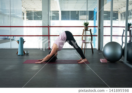 Woman practicing yoga downward dog pose in gym Woman practicing yoga downward dog pose in gym 141895598