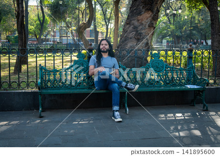 Man with long hair relaxing on green park bench Man with long hair relaxing on green park bench 141895600