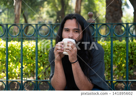 Man with long hair drinking coffee in park Man with long hair drinking coffee in park 141895602