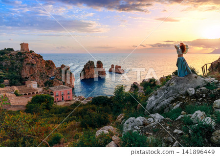 Woman in flowing dress posing back to camera in sunrise over Mediterranean sea and coastal village photography from above Woman in flowing dress posing back to camera in sunrise over Mediterranean sea and coastal village photography from above 141896449