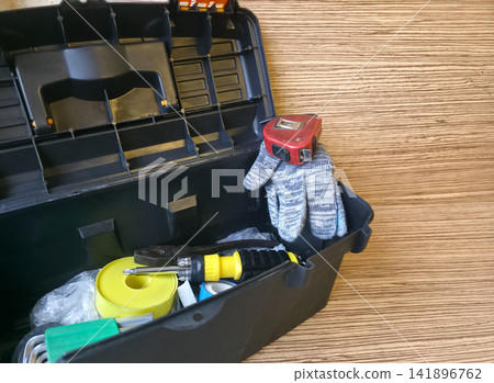 Open toolbox with pliers, tape measure, electrical tape and knit gloves on wood table, copy space. Handyman-for-an-hour concept, DIY repair kit, home maintenance, hardware advertising Open toolbox with pliers, tape measure, electrical tape and knit gloves on wood table, copy space. Handyman-for-an-hour concept, DIY repair kit, home maintenance, hardware advertising 141896762