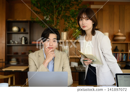 一名男子坐在電腦前，一名女子站著。 141897072
