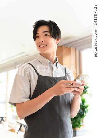 A male store clerk, holding a smartphone, is serving customers with a smile. A male store clerk, holding a smartphone, is serving customers with a smile. 141897128