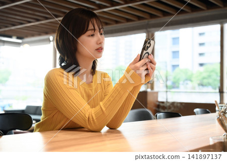 A woman looking at her smartphone, alone in a cafe. A woman looking at her smartphone, alone in a cafe. 141897137