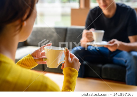A man and a woman holding coffee cups are having a conversation in a cafe. A man and a woman holding coffee cups are having a conversation in a cafe. 141897163