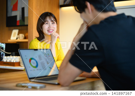 一位面帶微笑的女士帶著筆記型電腦在咖啡館與人交談。 一位面帶微笑的女士帶著筆記型電腦在咖啡館與人交談。 141897167