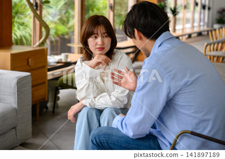 一對年輕情侶在咖啡館裡交談,他們神情嚴肅地討論著什麼事情。 一對年輕情侶在咖啡館裡交談,他們神情嚴肅地討論著什麼事情。 141897189