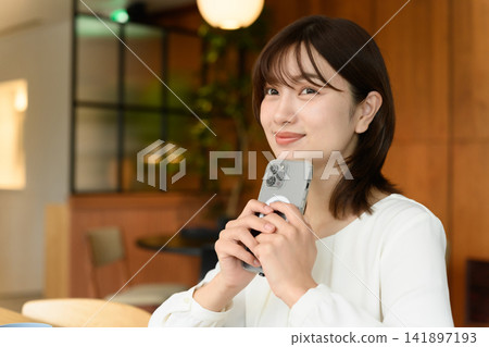 A woman holding a smartphone smiles and looks at the camera. A woman holding a smartphone smiles and looks at the camera. 141897193