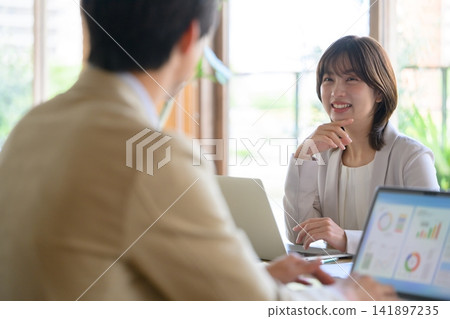 一位女士面帶微笑,正在使用筆記型電腦與一位男士開會。 一位女士面帶微笑,正在使用筆記型電腦與一位男士開會。 141897235