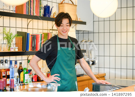 A young male staff member standing there wearing an apron. A young male staff member standing there wearing an apron. 141897295