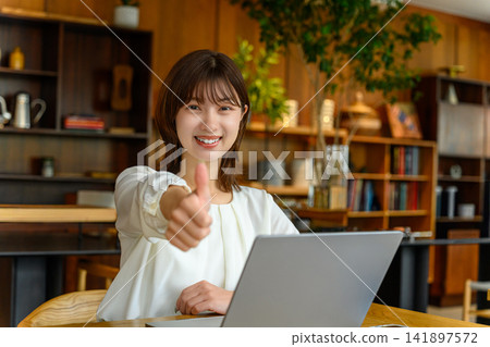 A woman giving a thumbs-up in front of her laptop. A woman giving a thumbs-up in front of her laptop. 141897572