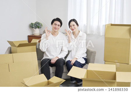 A couple makes peace signs in front of cardboard boxes during a move. A couple makes peace signs in front of cardboard boxes during a move. 141898330