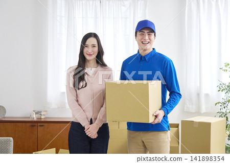 A smiling moving company worker and a woman holding cardboard boxes. A smiling moving company worker and a woman holding cardboard boxes. 141898354