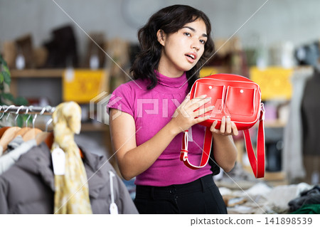 Female shopper chooses a fashionable handbag in clothing store Female shopper chooses a fashionable handbag in clothing store 141898539