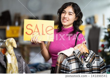 Happy female shopper holds a sign saying Sale in clothing store Happy female shopper holds a sign saying Sale in clothing store 141898541