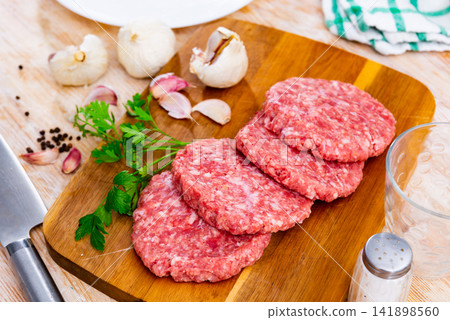 Formed raw burgers of pork and beef on a chopping board next to a whole garlic and parsley in the restaurant kitchen Formed raw burgers of pork and beef on a chopping board next to a whole garlic and parsley in the restaurant kitchen 141898560