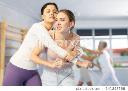 Group of women training to do painful hold in pairs during self-defense class Group of women training to do painful hold in pairs during self-defense class 141898566