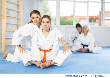 Girl before training martial arts performs stretching butterfly with couch help to warm up muscles. Girl before training martial arts performs stretching butterfly with couch help to warm up muscles. 141898612