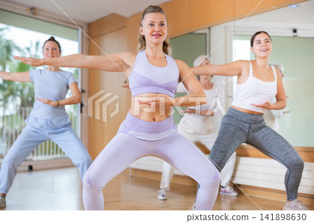 Excited sportive women of different ages dancing with legs wide apart in modern class of school for adults Excited sportive women of different ages dancing with legs wide apart in modern class of school for adults 141898630