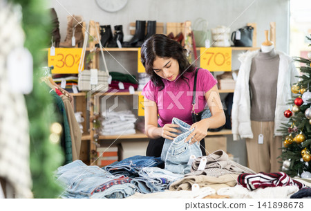 Asian woman chooses jeans trousers in clothing store before Christmas Asian woman chooses jeans trousers in clothing store before Christmas 141898678