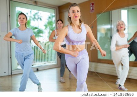 Excited positive women of different ages performing modern dancing exercises in school for adults Excited positive women of different ages performing modern dancing exercises in school for adults 141898696