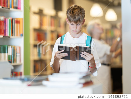 Teenage boy choosing books from display case table in bookstore Teenage boy choosing books from display case table in bookstore 141898751