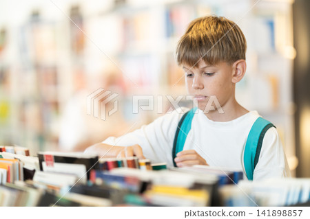 Teenage boy choosing books from display case table in bookstore Teenage boy choosing books from display case table in bookstore 141898857