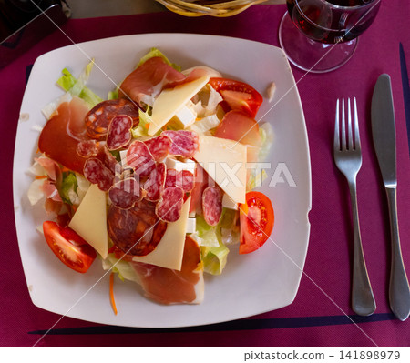 Catalan salad with sausage, cheese and vegetables served in the plate Catalan salad with sausage, cheese and vegetables served in the plate 141898979