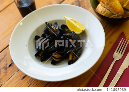 Steamed mussels in shells with lemon wedge on plate Steamed mussels in shells with lemon wedge on plate 141898989