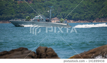 Naval patrol boat cruising through coastal waters on a sunny day against a lush green mountain backdrop Naval patrol boat cruising through coastal waters on a sunny day against a lush green mountain backdrop 141899438