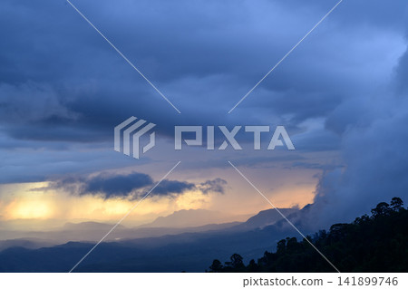 Mountain landscape at sunset. Dark, rainy clouds, with golden light illuminating the distant horizon and mist drifting across mountain peaks Mountain landscape at sunset. Dark, rainy clouds, with golden light illuminating the distant horizon and mist drifting across mountain peaks 141899746