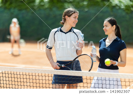 Two girls with bottles of water rest during break between tennis games Two girls with bottles of water rest during break between tennis games 141902307