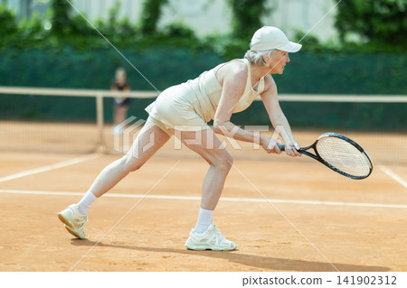 Senior female athlete plays tennis on open court with young opponent Senior female athlete plays tennis on open court with young opponent 141902312